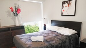 Et soveværelse med en seng, et natbord, en lampe, en vase med blomster og et maleri på væggen.