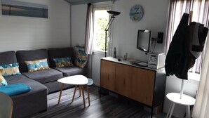 A living room with a grey sofa, a small white table, a wooden cabinet, a TV, and a lamp. - Holiday residence near the beach and the pyla dune (Gujan Mestras)