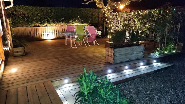 A wooden deck with outdoor seating and a planter with plants. - Holiday residence near the beach and the pyla dune (Gujan Mestras)