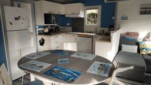 A compact kitchen with white cabinets, a microwave, and a coffee maker. There's a dining table with placemats featuring coastal scenes. - Holiday residence near the beach and the pyla dune (Gujan Mestras)