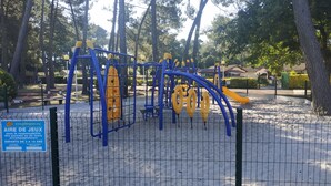A playground with climbing structures and a slide, surrounded by trees and a fenced area. - Holiday residence near the beach and the pyla dune (Gujan Mestras)