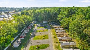 Un camping con vehículos recreativos y cabañas, rodeado de un bosque denso.