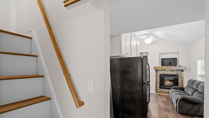 Un interior moderno con una escalera, un refrigerador negro, una chimenea y un sofá gris.