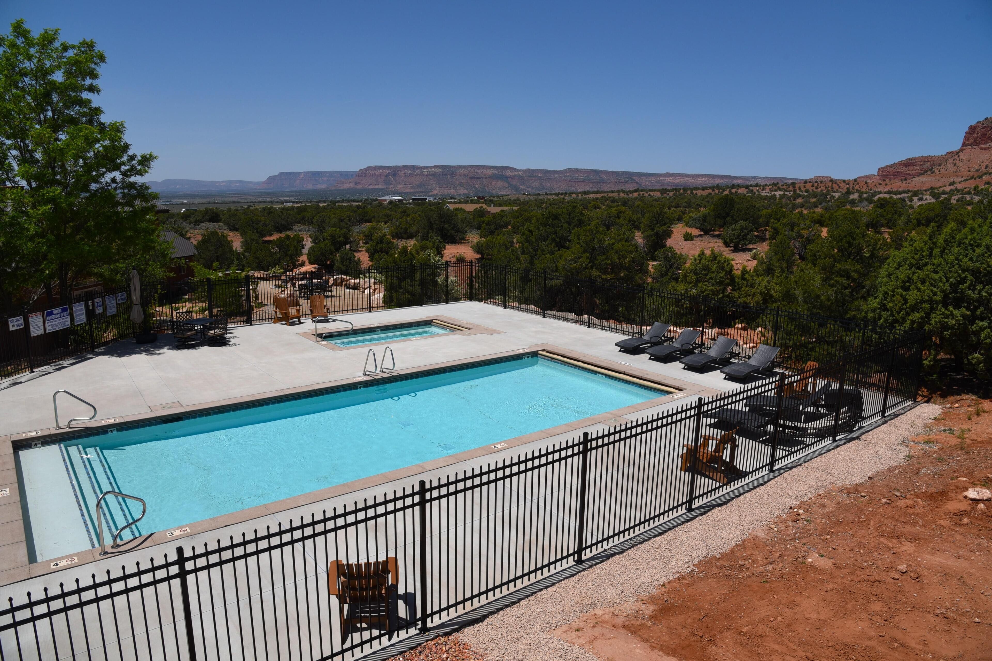 A rectangular swimming pool with a black metal fence, surrounded by trees and a clear view of distant mountains.