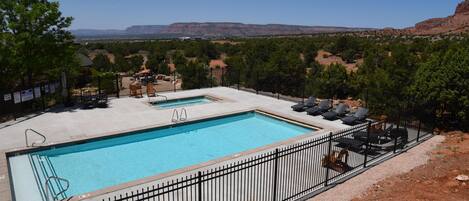 A rectangular swimming pool with a black metal fence, surrounded by trees and a clear view of distant mountains.