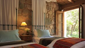 Un dormitorio con dos camas, paredes de piedra, una puerta de madera y vistas a zonas verdes.