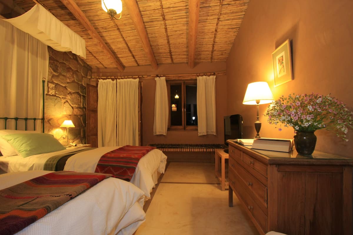 Una habitación de hotel acogedora con dos camas, un aparador de madera, un escritorio y una pared de piedra.