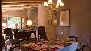 Un comedor con pared de piedra, techo de madera y una araña. Hay mesas de comedor dispuestas con platos y velas.