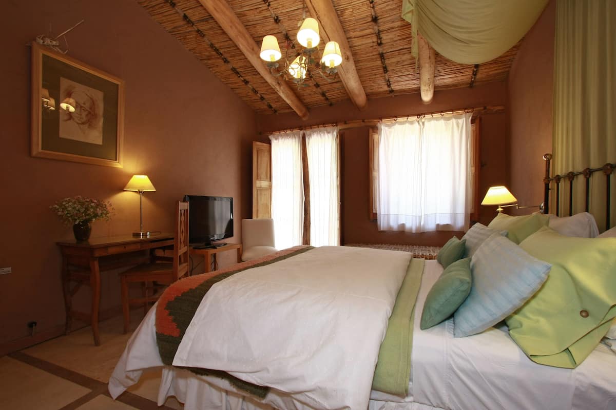 Un dormitorio con una cama, un escritorio con televisor, una silla y una lámpara.
