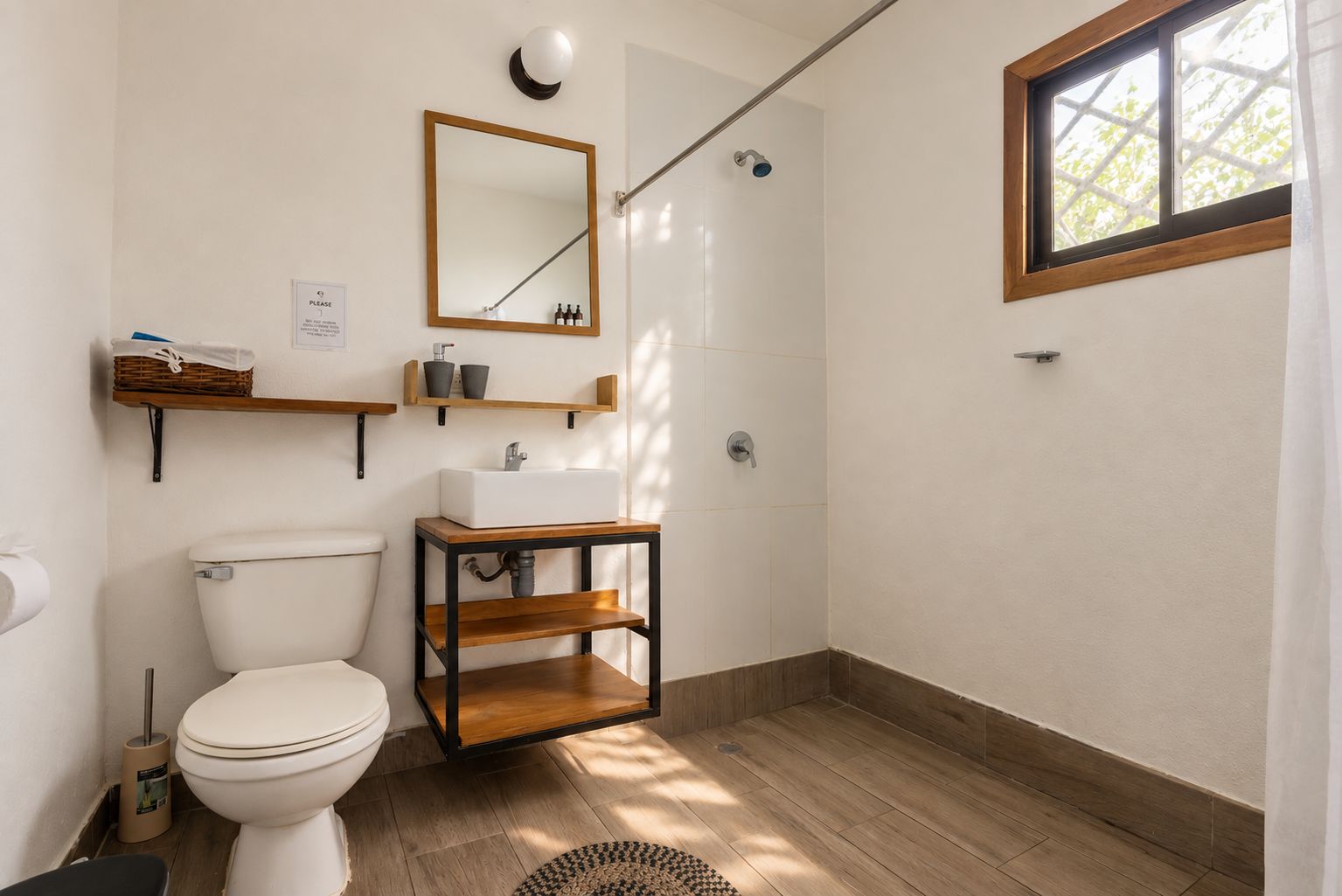 A bathroom with a toilet, sink, shower, and a window.