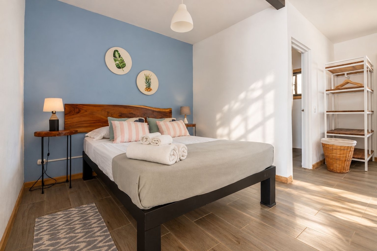 A bedroom with a bed, bedside tables, a hanging light fixture, a wooden headboard, and a wardrobe with shelves.