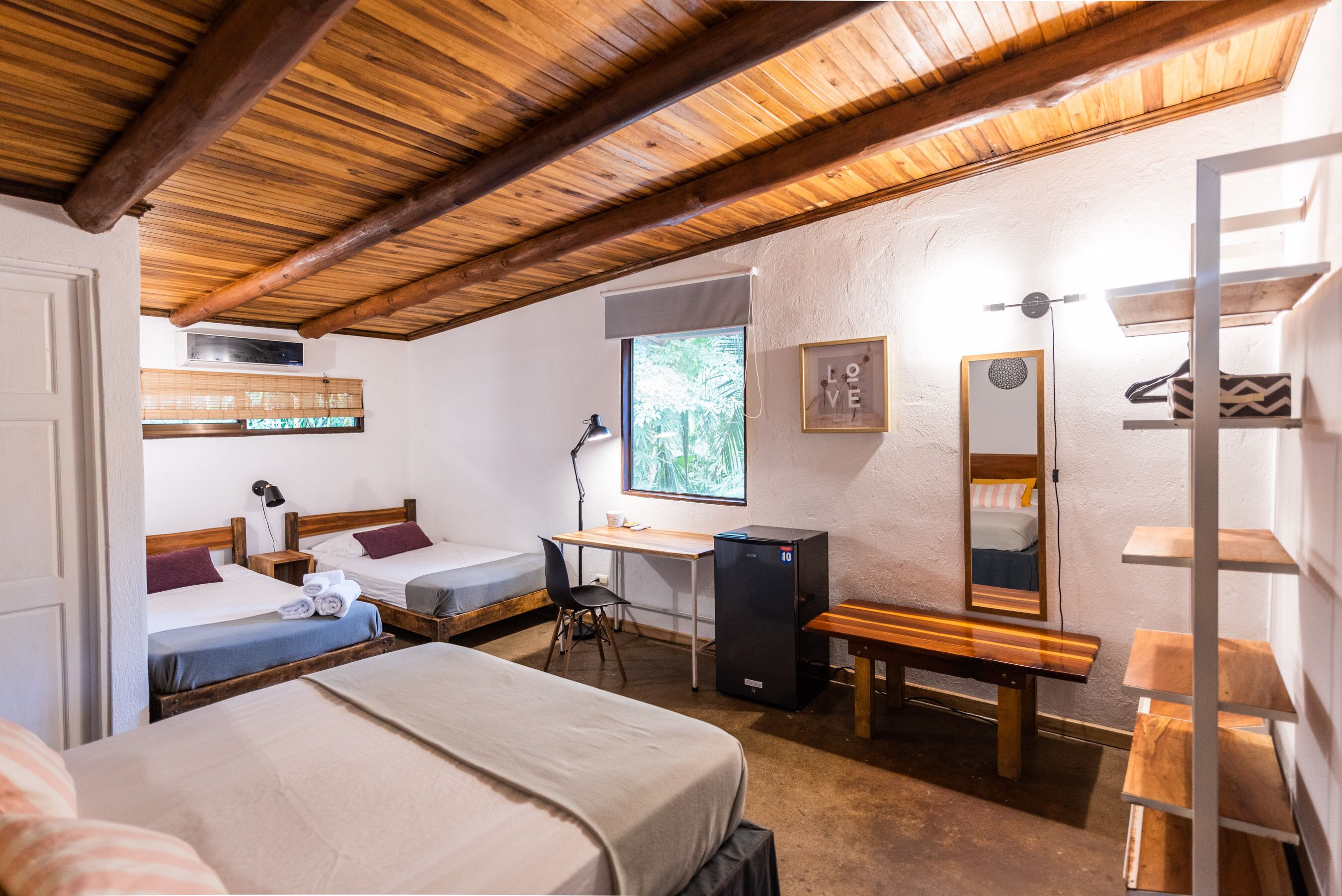 A cozy room with two beds, a desk, a computer, a mirror, and a shelf.