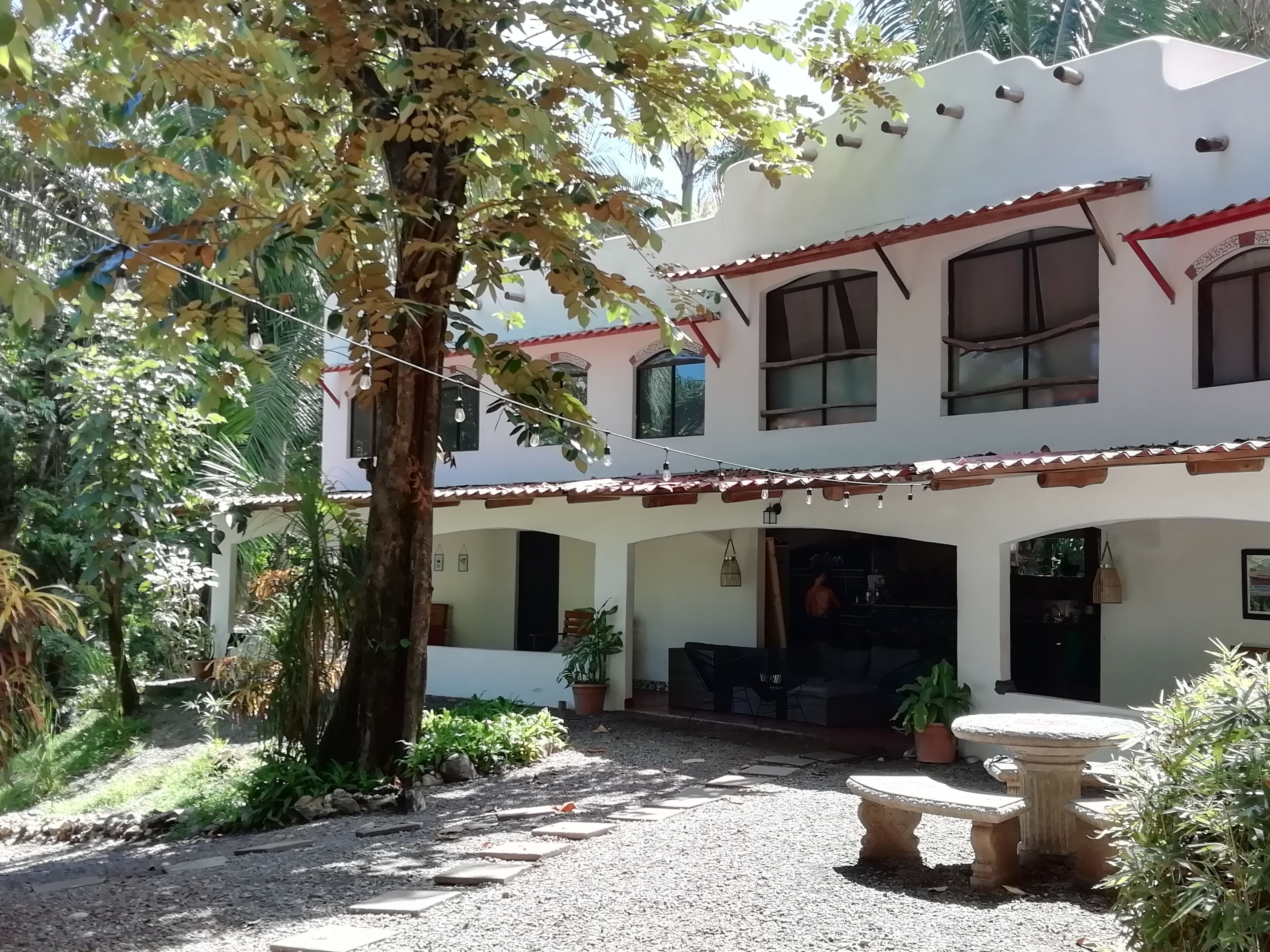 Un edificio de dos pisos con un patio, mobiliario exterior y plantas en macetas.