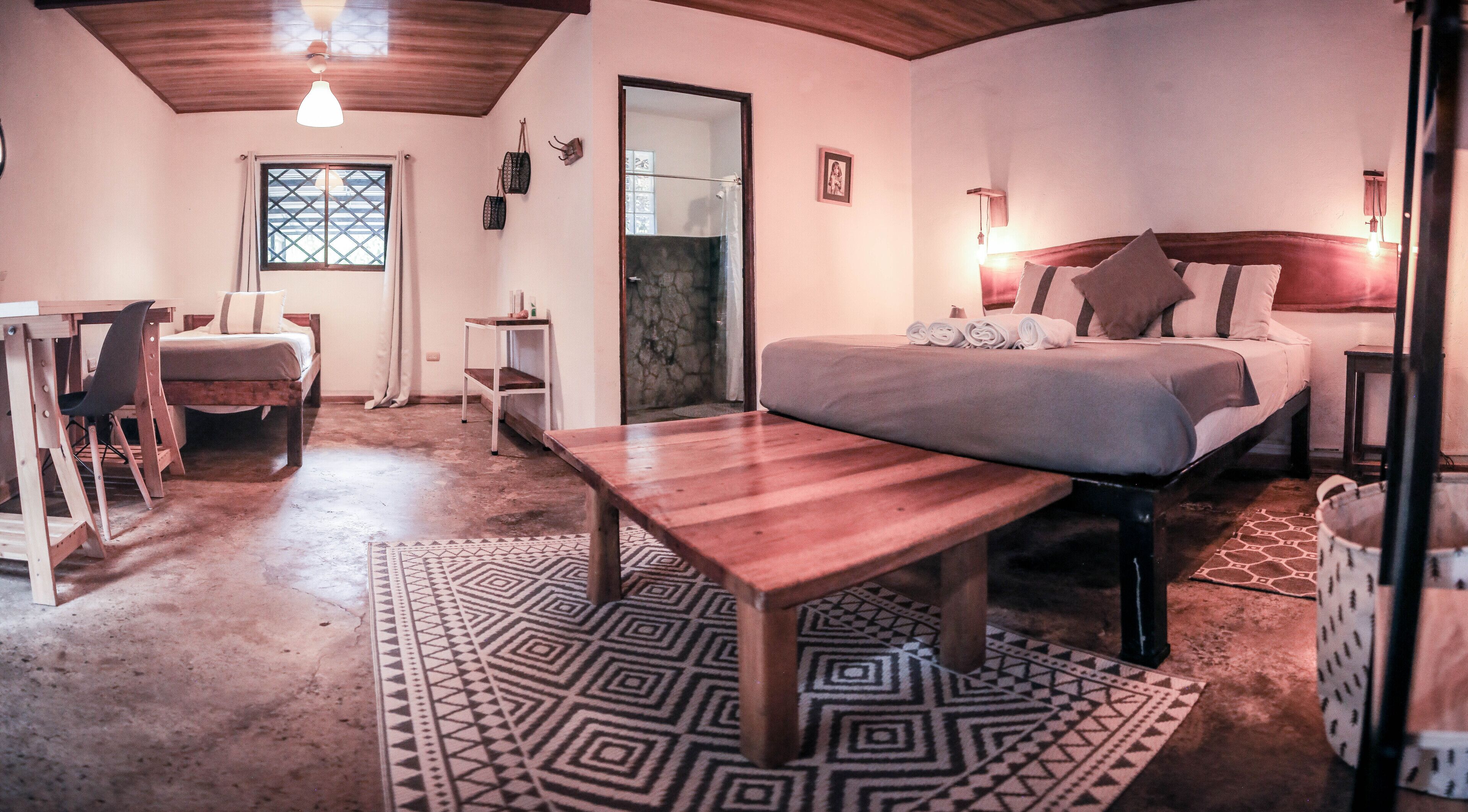 Un dormitorio acogedor con una cama de madera, un escritorio pequeño y una silla. Hay una ventana con vistas, un espejo y una alfombra estampada.