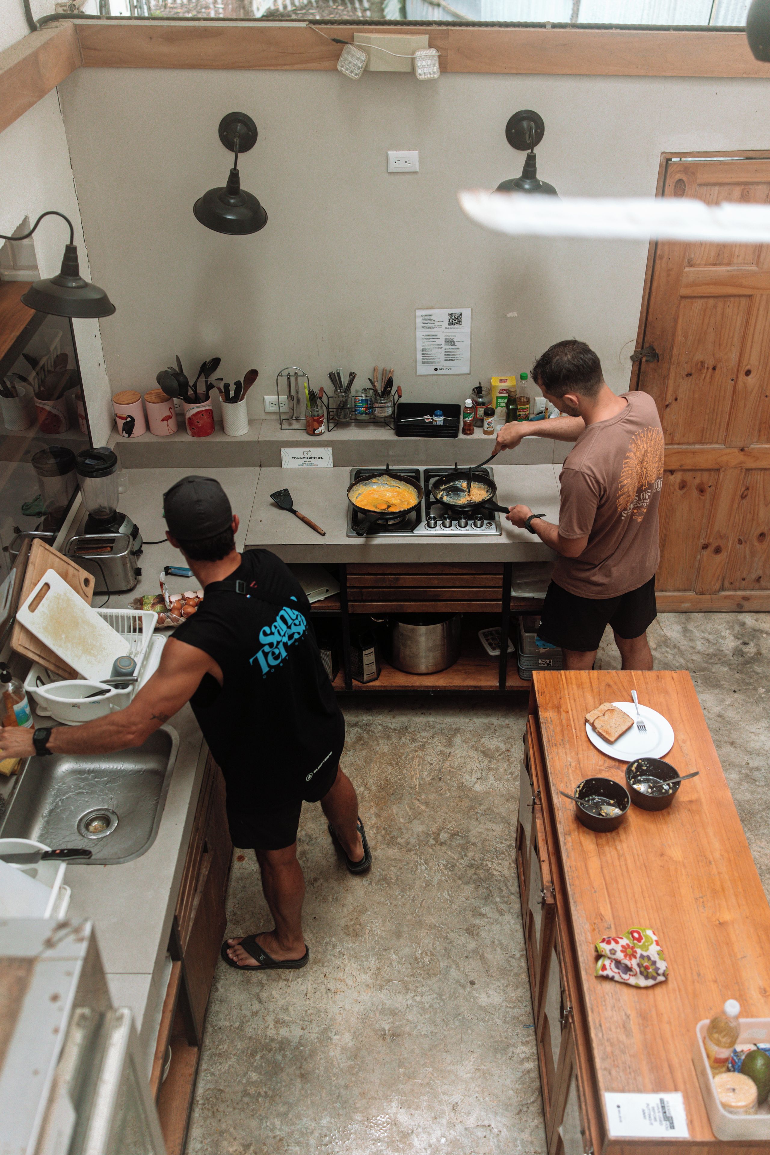 A kitchen with two people cooking, a sink, a stove, and various kitchen utensils.