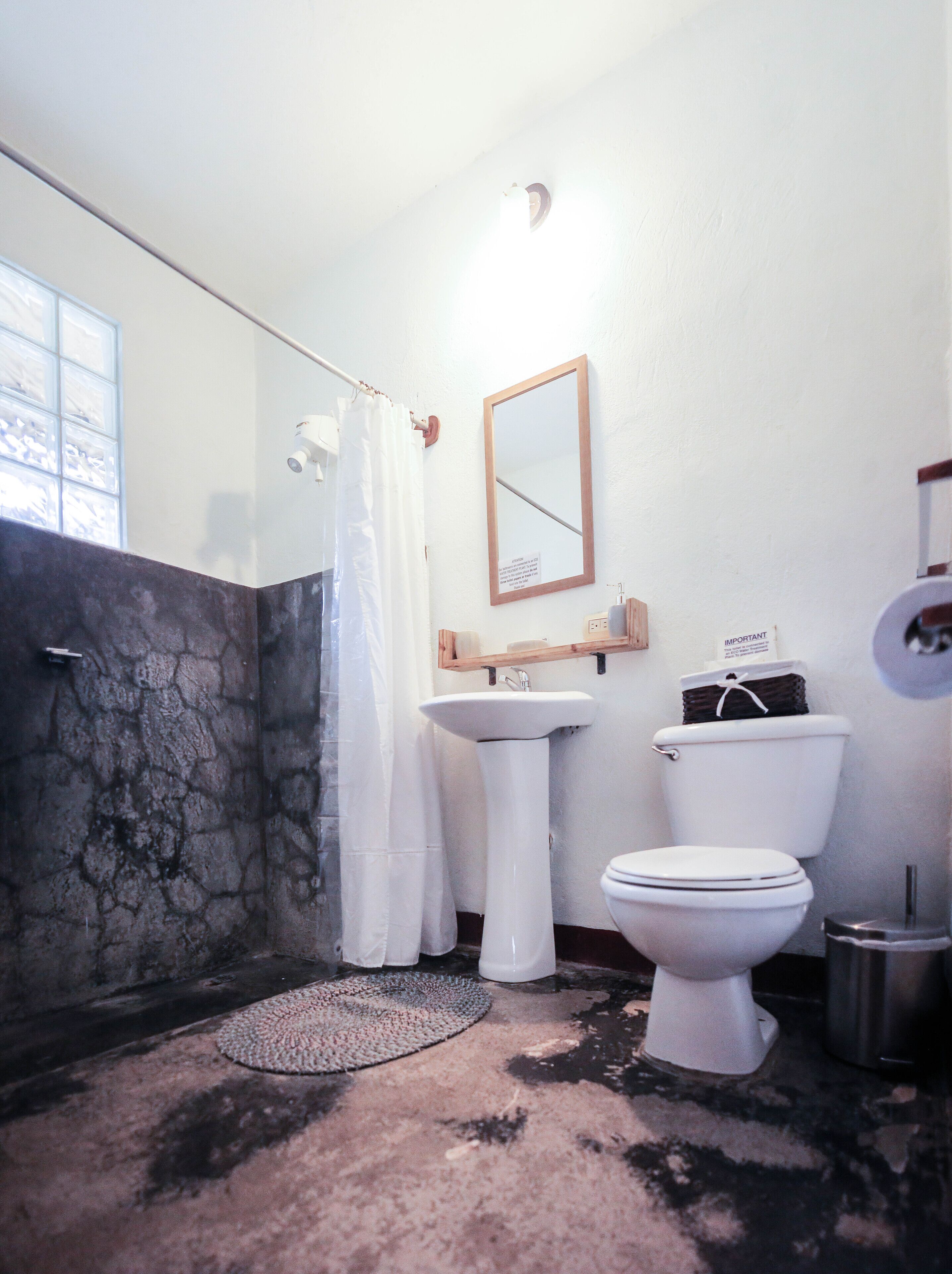 A bathroom with a stone wall, a white sink, a toilet, and a mirror.