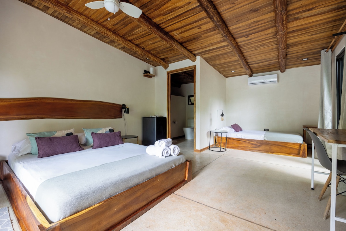 A hotel room with a large bed, a smaller bed, a desk, and a ceiling fan.