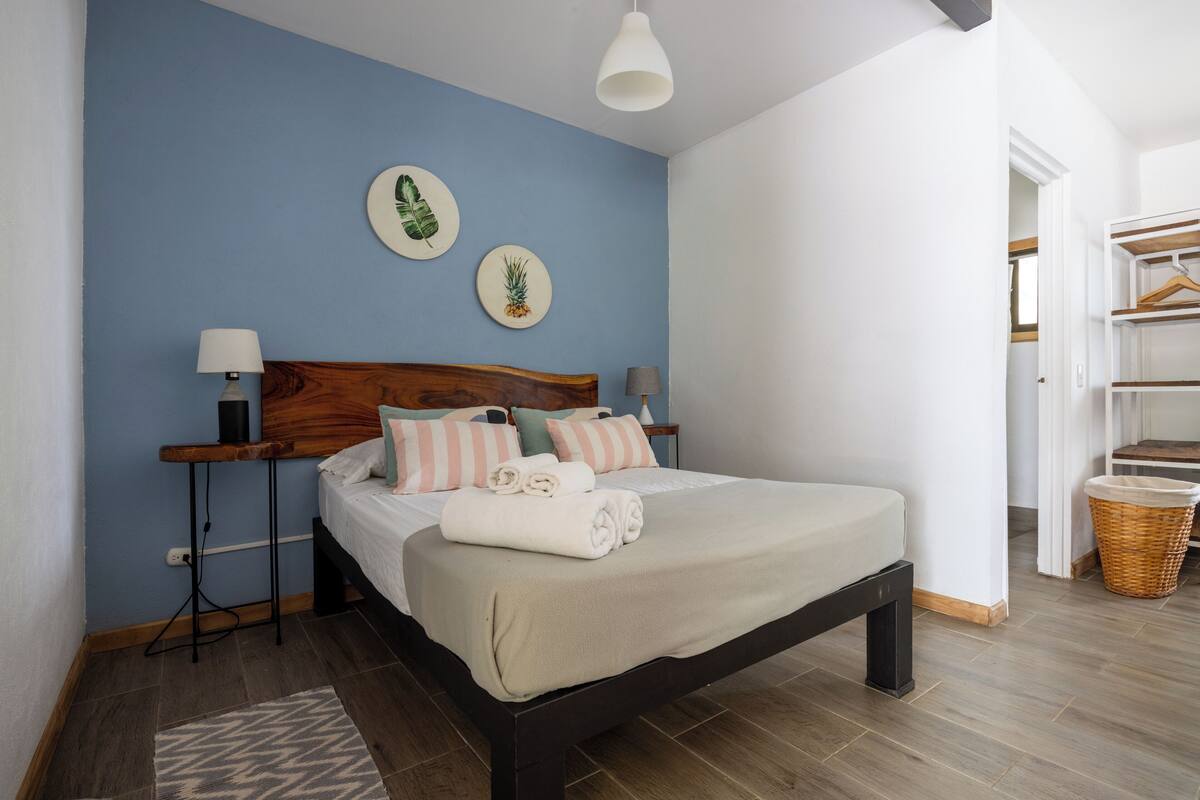 Un lit bien fait, avec une tête de lit en bois, deux lampes fixées au mur et un mur bleu orné de deux assiettes décoratives.