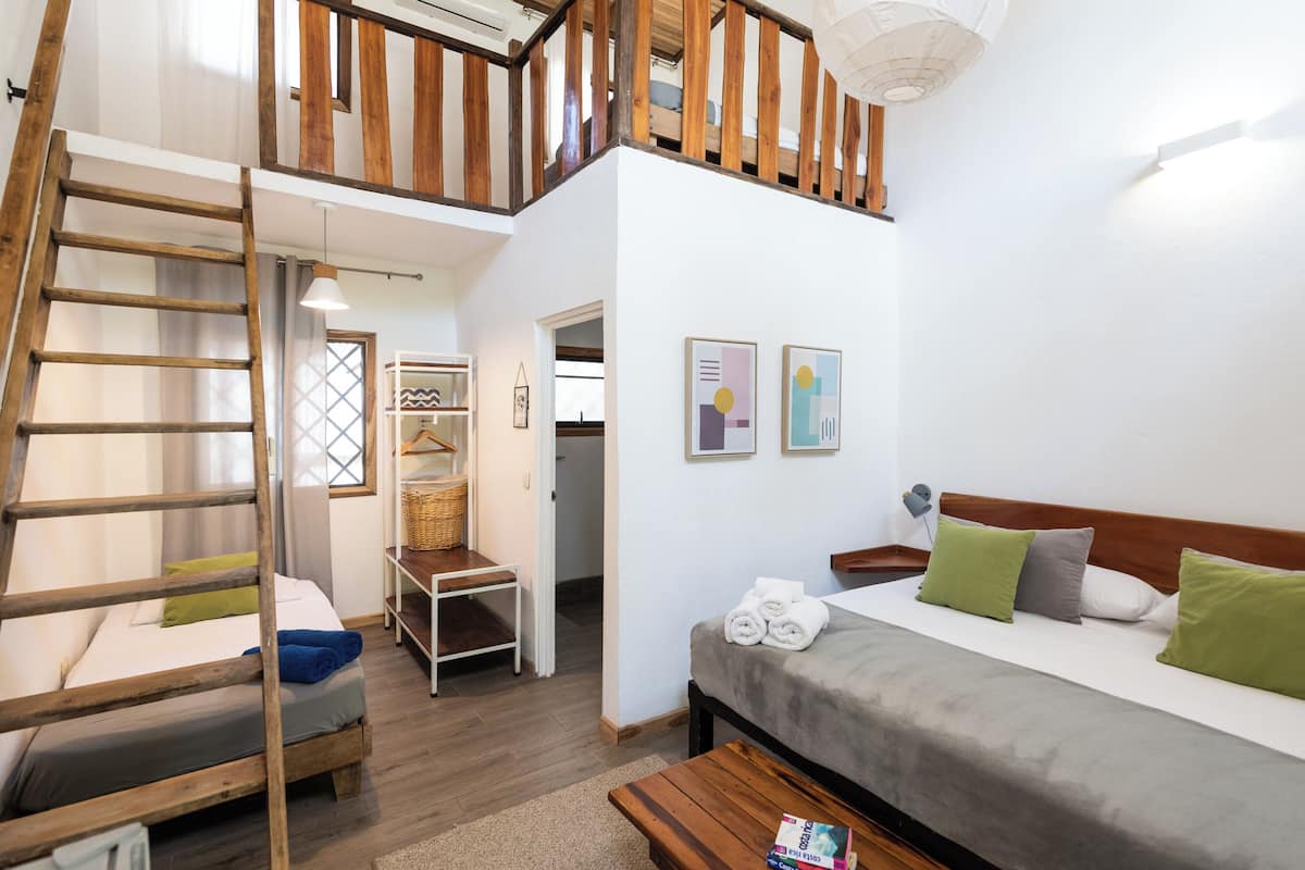 Une chambre de style « loft », avec une échelle en bois, un lit superposé, un canapé-lit et une petite table.