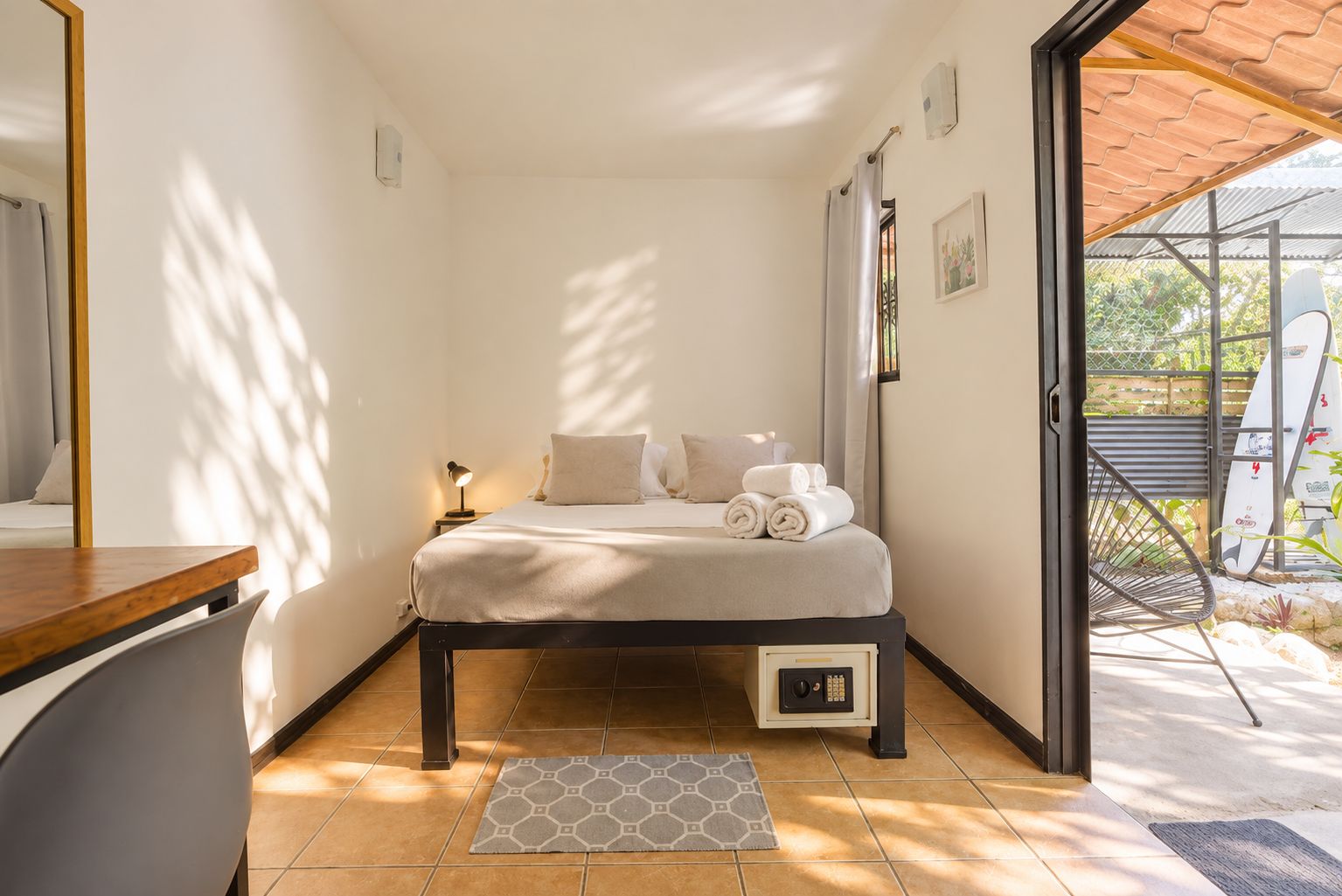 A bedroom with a bed, bedside table, and a view of the outside.
