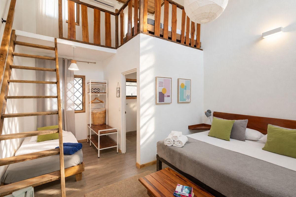 A bedroom with a bed, a wooden ladder, a bedside table, a hanging light, and a wall-mounted shelf.