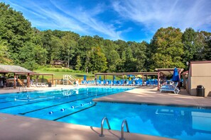Une piscine dotée de plusieurs couloirs, de chaises longues et de parasols, entourée d’une zone boisée.