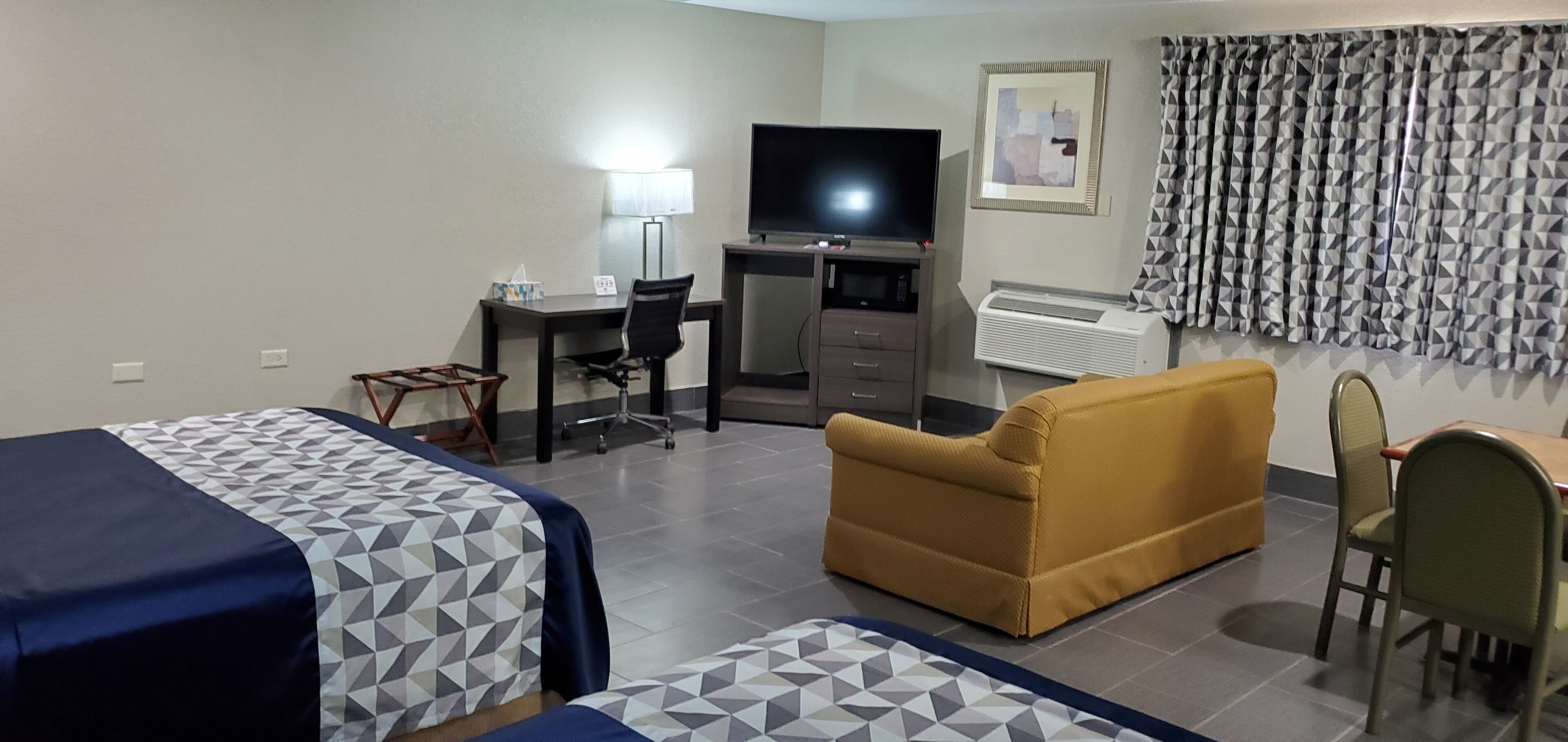 Habitación de hotel con dos camas, un sofá, un escritorio con televisor, una silla, una mesa y una cortina estampada.