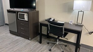 A hotel room with a desk, a chair, a TV, a microwave, a refrigerator, a phone, and a lamp. - Crescent Park Motel & Suites (Littlefield)