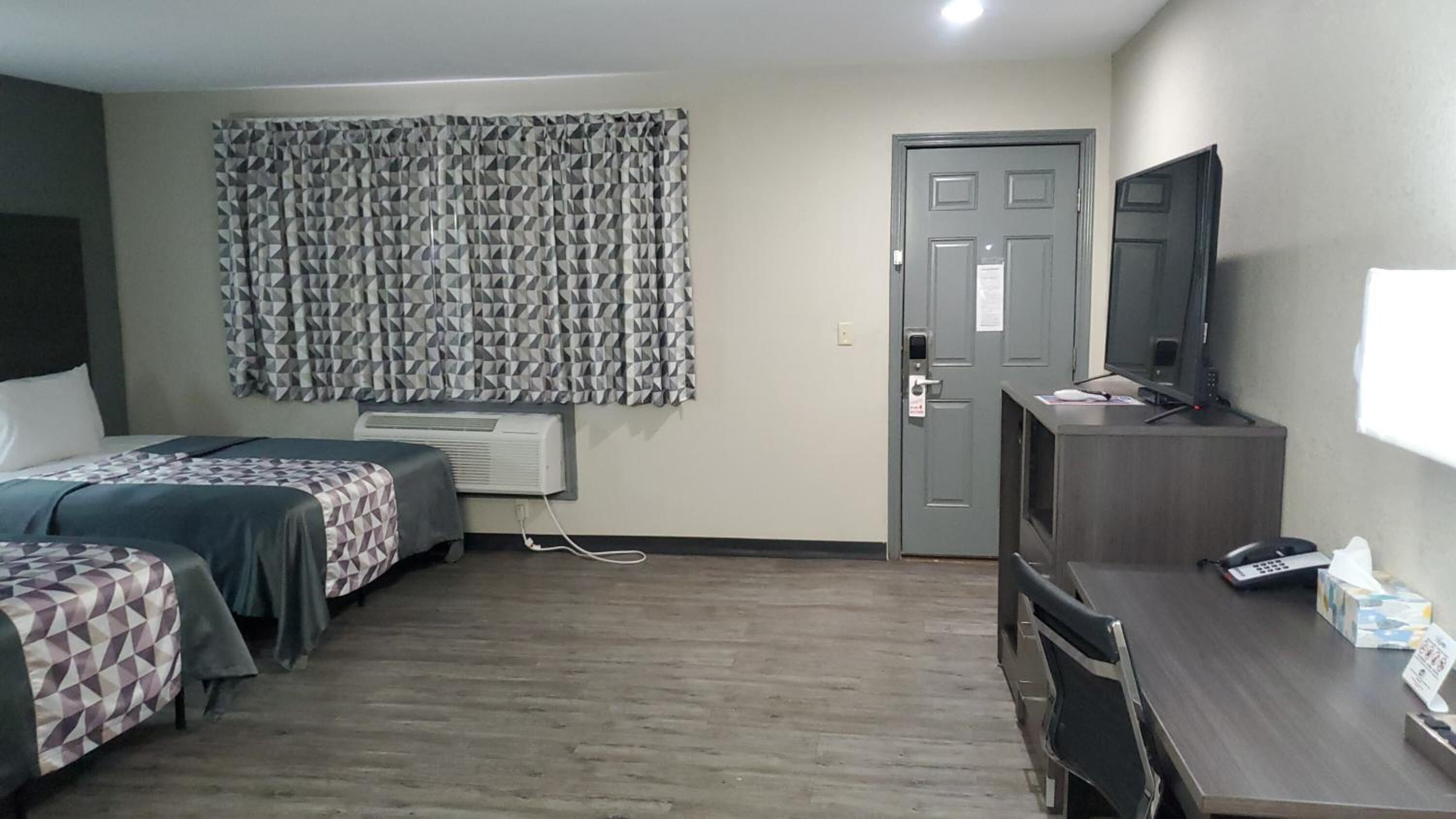 Une chambre d’hôtel avec deux lits, un bureau avec un ordinateur, une télévision et une porte.