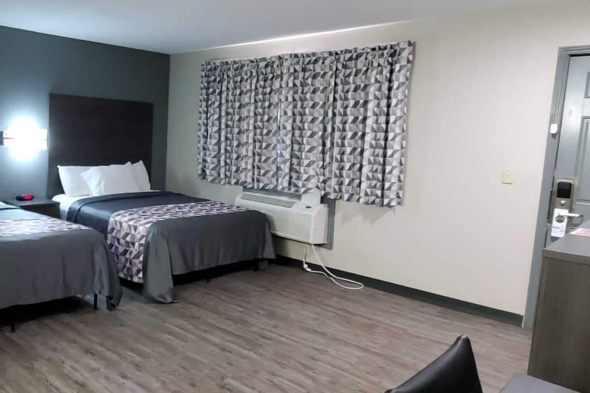 A hotel room with two beds, a desk, a chair, and a window with patterned curtains.
