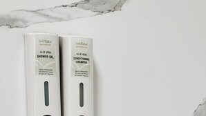 A marble wall with two bottles of Natura Aloe Vera Shower Gel and Conditioner Shampoo. - Crescent Park Motel & Suites (Littlefield)