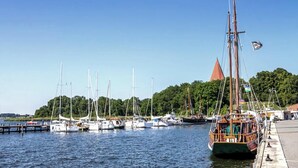 Een jachthaven met verschillende zeilboten afgemeerd, een opvallend gebouw met een rood dak, en weelderige begroeiing op de achtergrond.