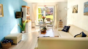 Een woonkamer met een bank, een televisie, een eettafel met stoelen en uitzicht op de omgeving.