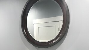 Consola de madera oscura con un espejo redondo encima, sobre un pared de color gris claro.