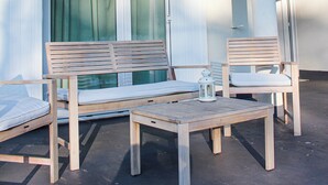 Un espace extérieur abrité, doté de mobilier en bois et d’une table, situé sous une structure recouverte d’un toit en tuiles.