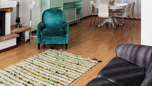 Un salon comprenant un fauteuil turquoise, un canapé noir, un coin repas avec une table et des chaises, et une bibliothèque.