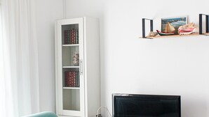 Un salon avec un canapé de couleur turquoise, un meuble blanc rempli de livres, un téléviseur à écran plat et une étagère ornée d’objets décoratifs.