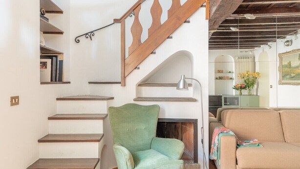 A staircase with wooden steps and a wooden railing, a green armchair, a beige sofa, and a fireplace in the background. - Joy Apartment 2 - Rome - Trastevere (Roma)