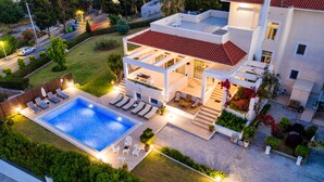 Et moderne hus i to etager med swimmingpool, udendørs møbler og en velplejet have.
