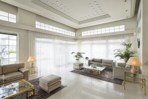 A spacious living room with a high ceiling, large windows, and modern furniture.