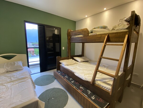 A bunk bed room with a wooden ladder, a white bed, and a view through a glass door.