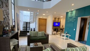 Un vaste espace de vie aménagé avec des meubles en osier, un téléviseur à écran plat et un escalier menant à un niveau supérieur.