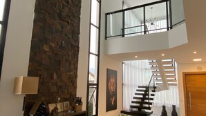 Un vaste espace de vie doté d’un haut plafond, d’un mur d’accent en pierre, d’un escalier menant à l’étage supérieur et d’un aménagement de sièges confortable.
