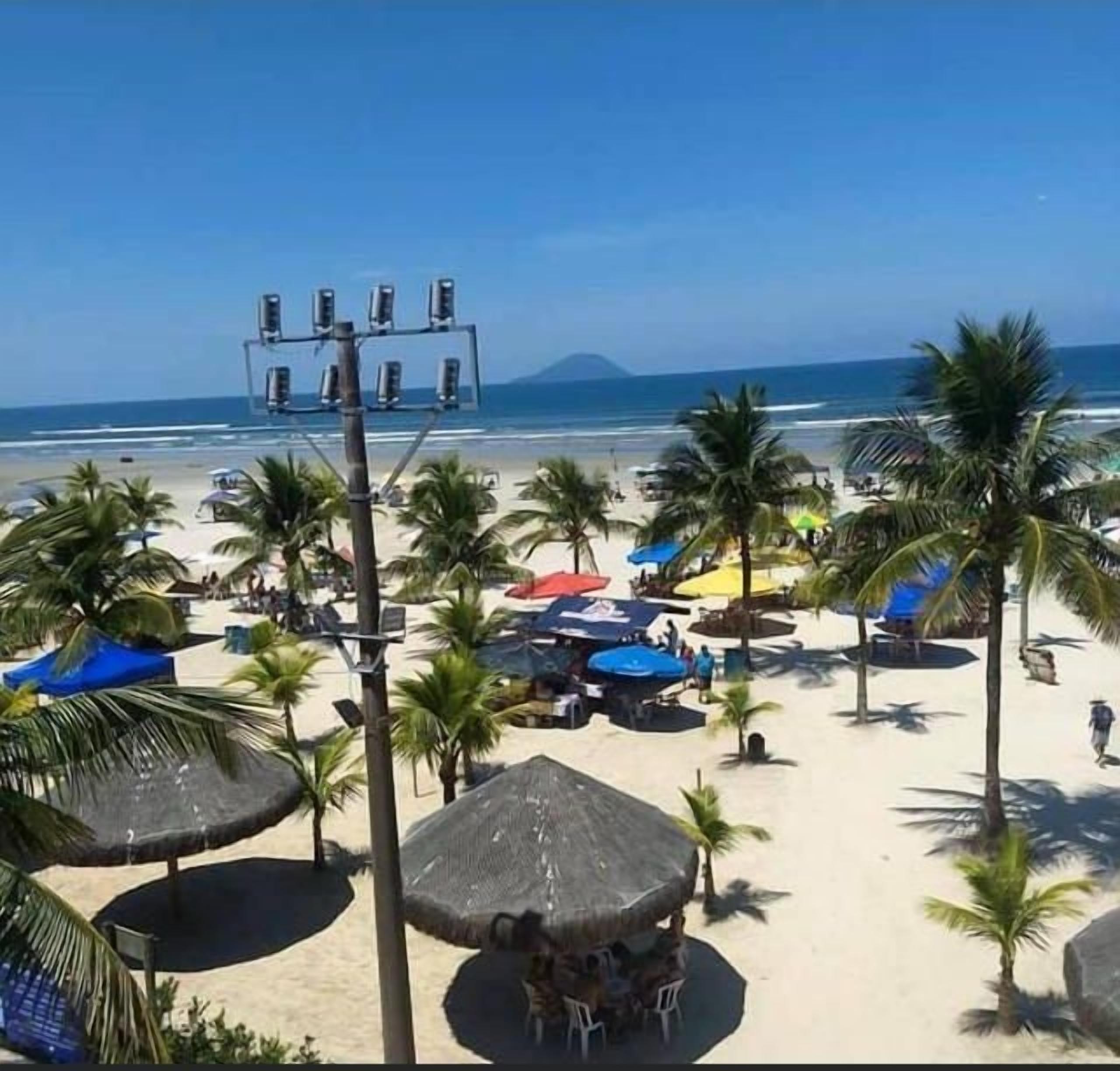 Une plage bordée de palmiers, avec des parasols et un ciel dégagé.