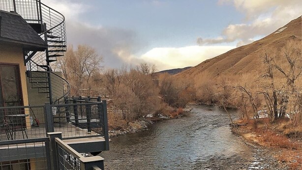 A riverside view from a balcony with a metal railing, a small table, and chairs. - This riverfront downtown condo boasts and open floor plan for kitchen, living room, and dining areas. Or step onto the balcony over the Arkansas River to hear the water rushing by. Oversized master suite has its own balcony and indoor sitting area. (Salida)