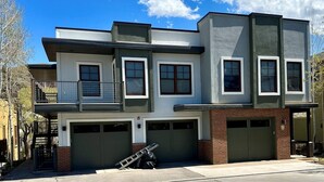 A modern two-story house with a balcony, two garages, and a ladder leaning against the garage. - This riverfront downtown condo boasts and open floor plan for kitchen, living room, and dining areas. Or step onto the balcony over the Arkansas River to hear the water rushing by. Oversized master suite has its own balcony and indoor sitting area. (Salida)