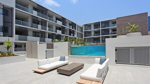 A modern outdoor lounge area with a pool, white sofas, and a wooden coffee table.