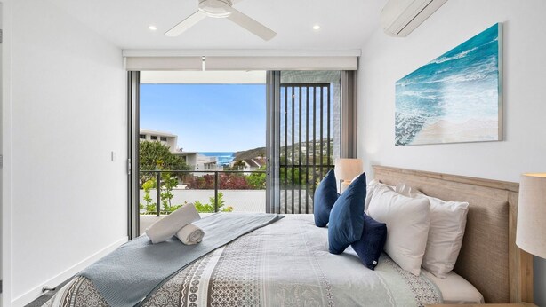 A bedroom with a bed, pillows, a nightstand, a lamp, and a painting of the ocean.