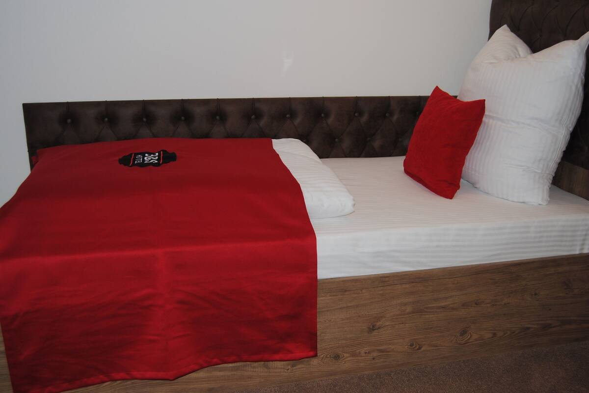A bed with a red blanket, white pillows, and a wooden headboard.