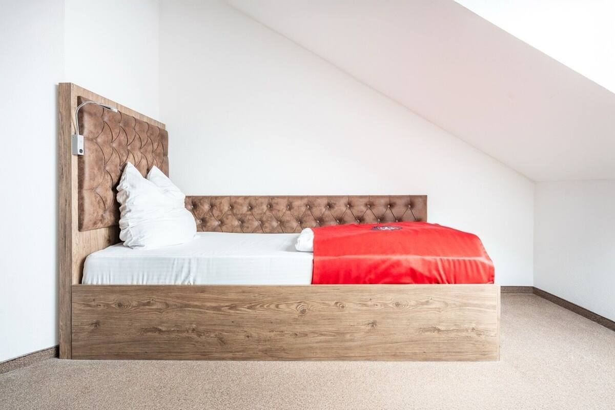 A modern loft bedroom with a wooden headboard, white bedding, and a red accent pillow.